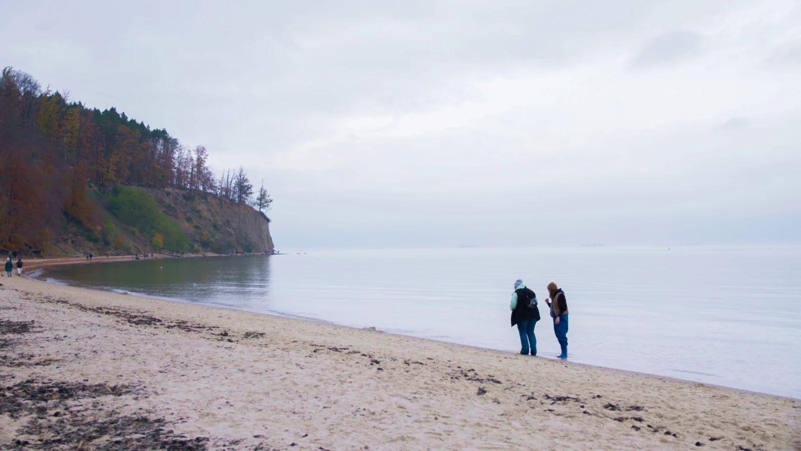 Dwie osoby na piaszczystej plaży pod klifem orłowskim, spokojna tafla Bałtyku w pochmurny dzień