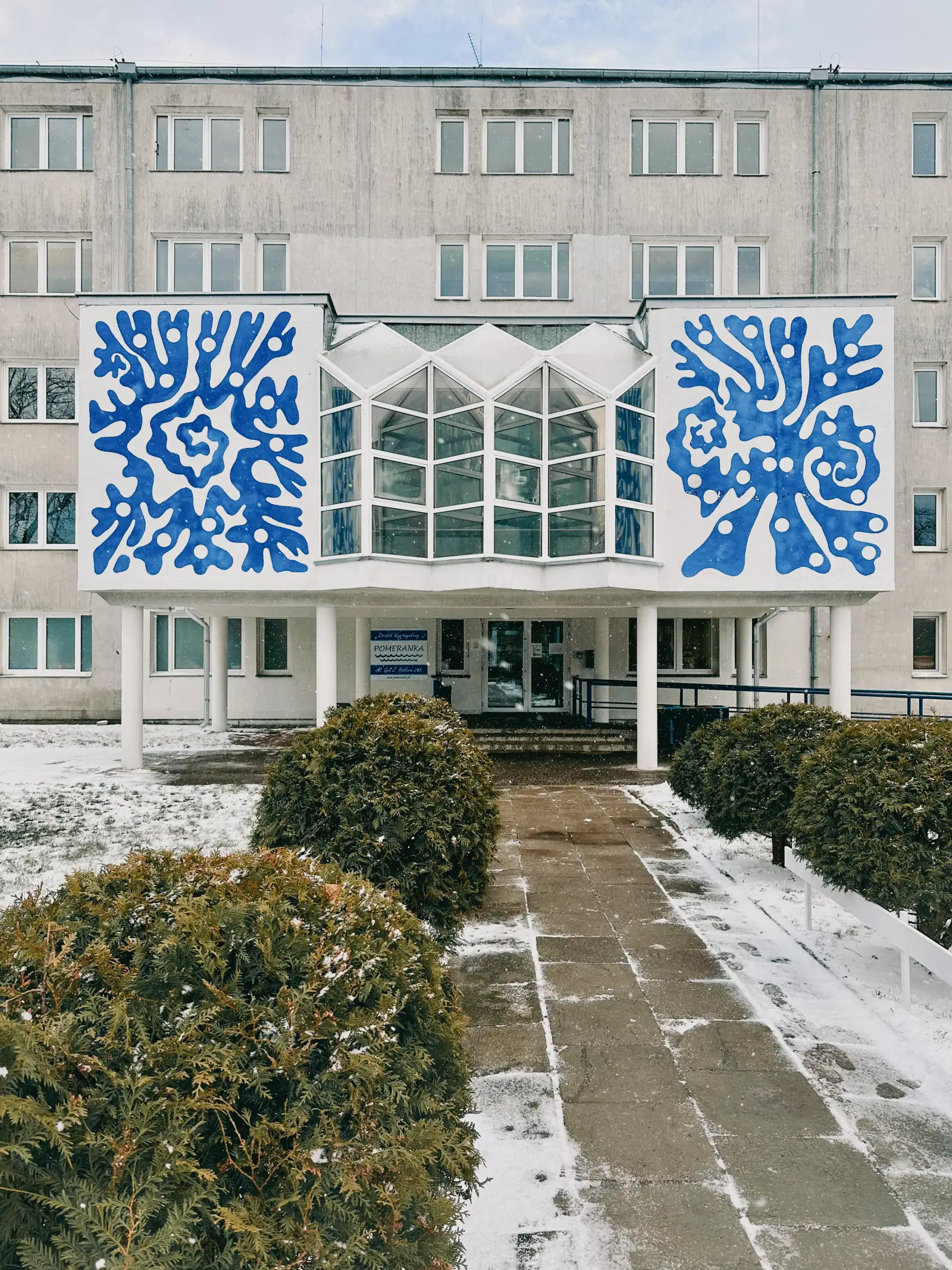 Dwa niebieskie murale w kształcie koralowców na białej fasadzie budynku zimą